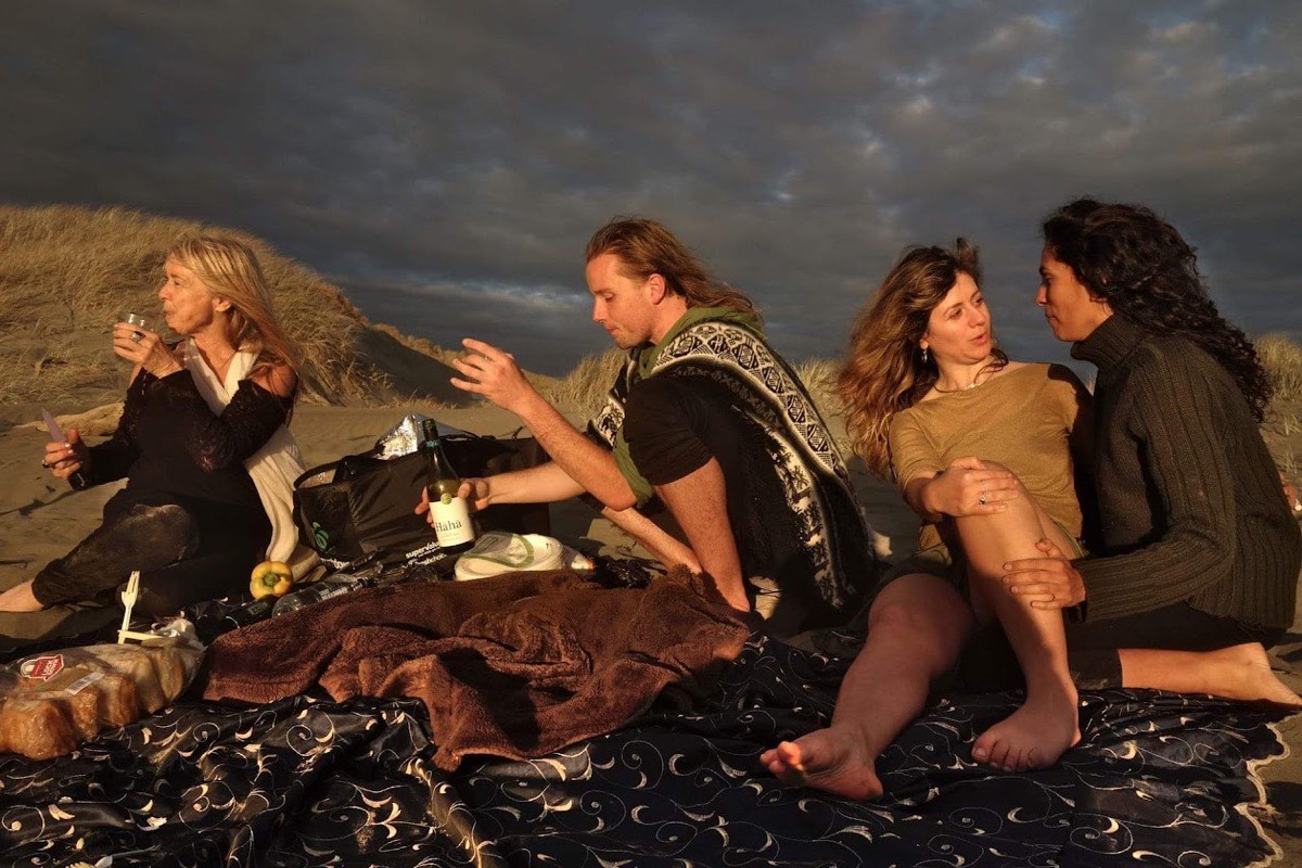 Four people sharing food and conversation on a beach at golden hour